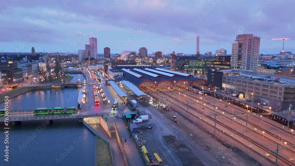 Train arrives at Malmo Centralstation and buses cross bridge, twilight aerial Train arrives at Malmo Centralstation and buses cross bridge, twilight aerial