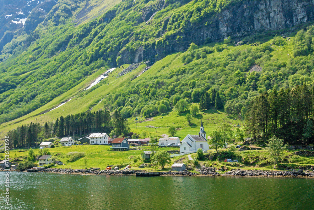 Obraz premium Quaint village of Bakka nestled along the coast of the fjord mountains and forest in Aurland from an angle