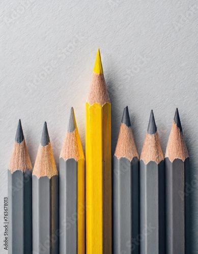 Gray colored pencils, one yellow colored pencil in one line on white paper background with copy space