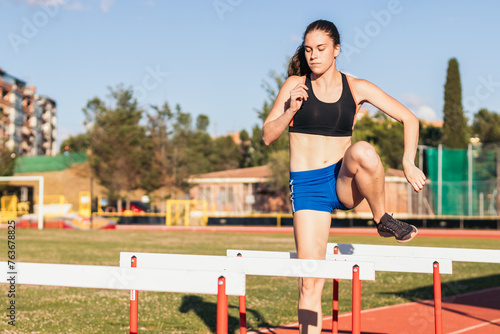 athlete training by jumping hurdles on an athletics track.