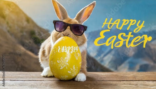Frohe Ostern Konzept Feiertag Grußkarte - Cooler Osterhase mit Sonnenbrille lehnt sich an ein großes bemaltes gelbes Osterei mit deutschem Text auf Tisc photo