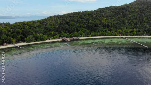 Island landscape with sandy beach and guesthouses, lush greenery, clear water. Aerial tilted shot. photo