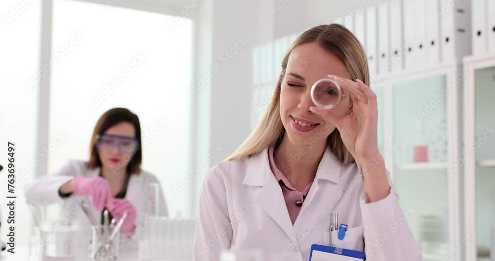 Smiling assistant looks through glass beaker in laboratory Smiling assistant looks through glass beaker in laboratory