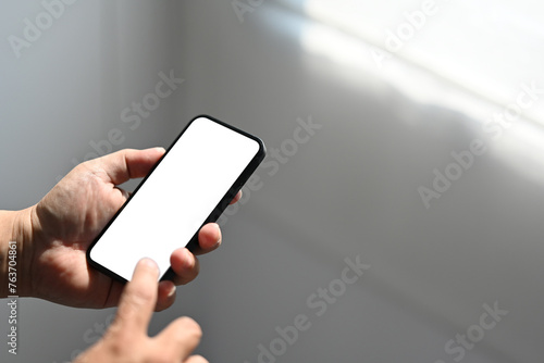 Man's hand using cellphone , reading an informations or email on the phone, Blurred background. Phone white screen mockup.
