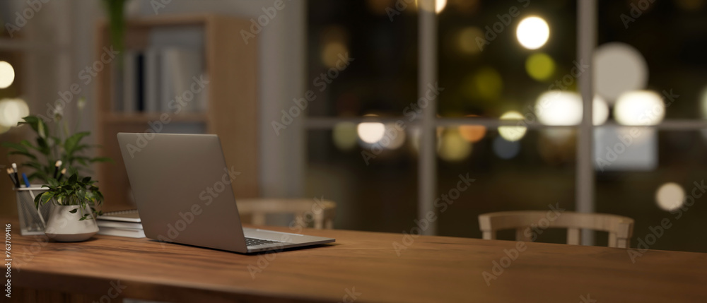 A back view image of a laptop on a dining table in a comfortable, minimalist dining room at night. A back view image of a laptop on a dining table in a comfortable, minimalist dining room at night.