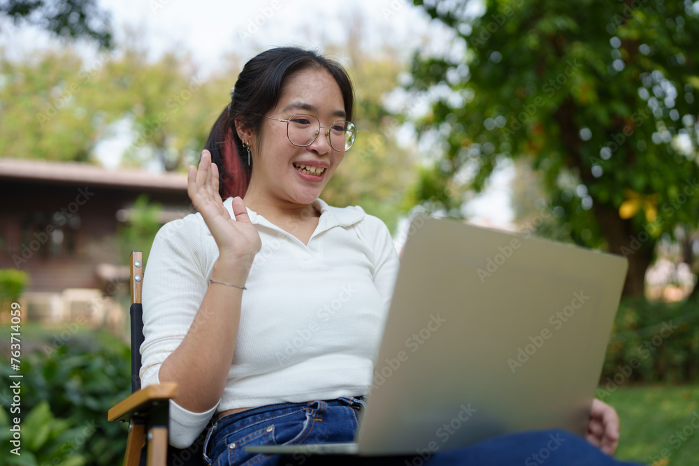 Young women wearing glasses wearing headphones reading a book Making diary notes Video calls via laptop online, relaxing, lifestyle, vacation, at the park Happily natural place. Young women wearing glasses wearing headphones reading a book Making diary notes Video calls via laptop online, relaxing, lifestyle, vacation, at the park Happily natural place.