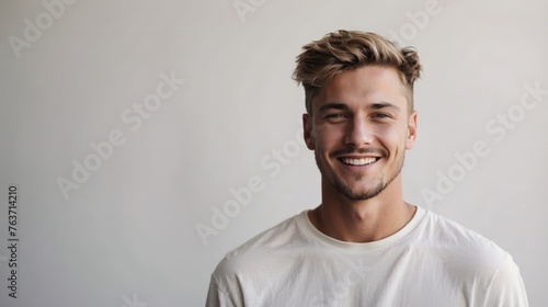 Portrait of young happy white caucasian man smiling standing in front of blank white wall looks in camera