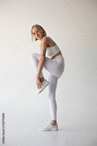 Beautiful blonde girl posing on a white background in white leggings and a white top