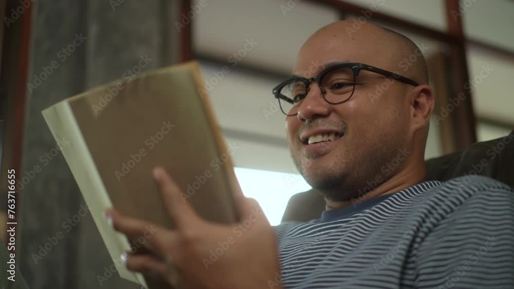 Leisure time of Asian man wearing eyeglasses holding and reading book sitting on sofa in living room. People male stay home part time relax at home.
Leisure time of Asian man wearing eyeglasses holding and reading book sitting on sofa in living room. People male stay home part time relax at home.