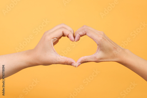 Female hand and male hand making a heart shape by fingers  isolated on yellow background.