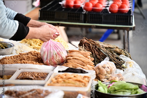A close-up shot of a pickled vegetable stall in the market, with various pickled food items displayed. The vendor is packaging items purchased by customers.