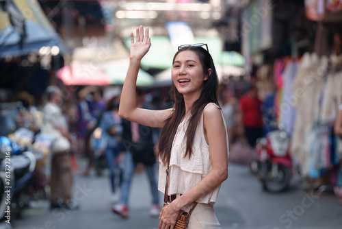 A cheerful, beautiful Asian woman wanders the streets, waving hello, searching for delicious street food. backpacker Holiday travel ideas, lifestyle.