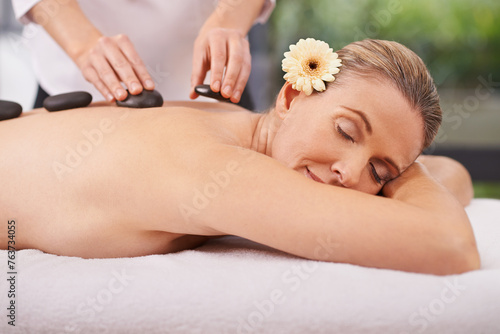 Woman, hands and hot stone massage with masseuse at spa, flower for natural treatment and wellness with zen. Calm, peace and luxury bodycare with warm rocks for detox, self care and holistic healing