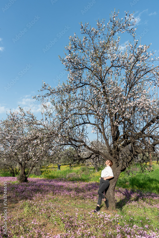 Young woman leaning and relaxing under almond blooming tree enjoying spring.