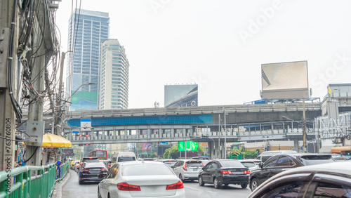 1 January 2024 in Bangkok, Thailand Image of traffic starting to move through a red light intersection. At the top is a skywalk. Surrounded by many tall buildings.