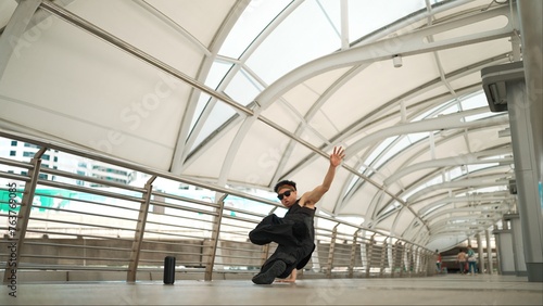 Skilled handsome hipster perform street dancing at narrow corridor. Professional hip hop dancer show b-boy step at corridor at urban city while wearing stylish cloth. Outdoor sport 2024. Sprightly.