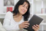 mature brunette woman sitting on sofa using digital tablet