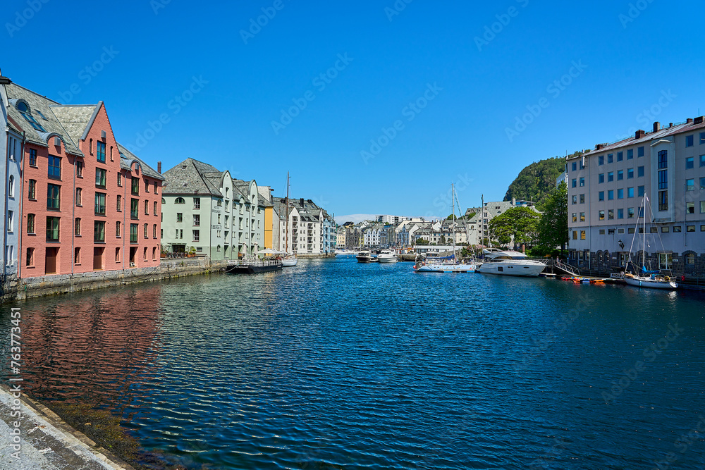 beautiful port in the city center of Alesund along the coastline of the atlantic ocean in Norway on a sunny day with blue water and colorful houses.