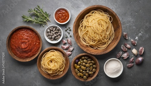Ingredients for cooking spaghetti anchovy pasta salt in wooden bowl, olives, anchovies and tomato sauce over grey texture background