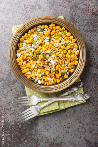 Homemade Mexican Street Corn Esquites Salad with jalapeno, cilantro, Cotija cheese, onion and spices seasoned with sour cream close-up on the plate on the table. Vertical top view from above