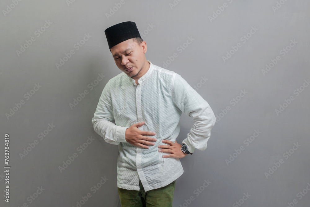 Asian Muslim man holding back hunger and waiting for the time Asian Muslim man holding back hunger and waiting for the time