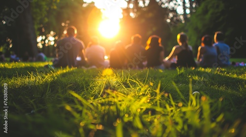 A group of people sitting on grass in the park,enjoying outdoor activities together at sunset. photo