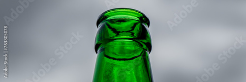 A striking low angle shot presents the bottleneck of an empty green beer bottle set against a cloudy sky, creating a captivating contrast and leaving ample room for creative copy or design elements.