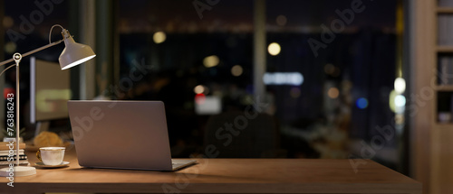 Quadro em tela A laptop in a contemporary office room at night illuminated by dim lights from a table lamp