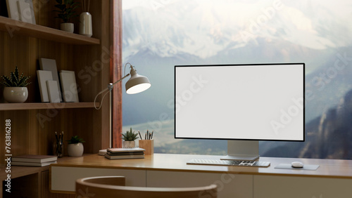 A home office features a computer mockup against the window with a view of snow-capped mountains. © bongkarn