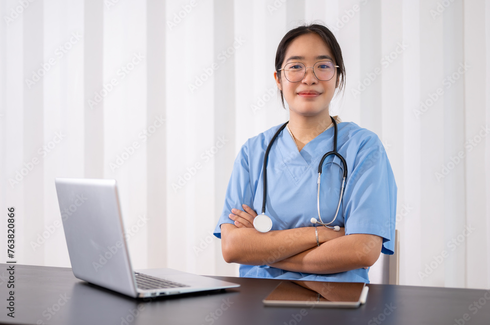 A professional and confident Asian female doctor sitting with her arms crossed at her desk. A professional and confident Asian female doctor sitting with her arms crossed at her desk.