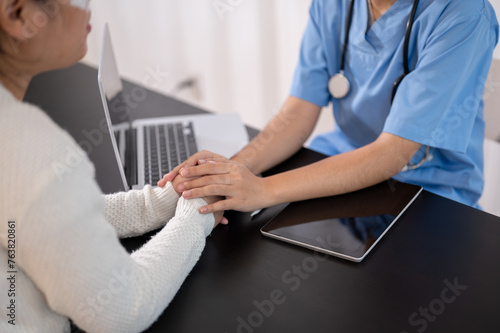 A doctor is touching a patient's hands on the table, comforting a patient during the consultation. © bongkarn