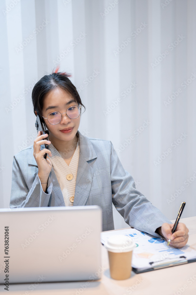 A businesswoman is talking on the phone, taking notes, and reading information on her laptop. A businesswoman is talking on the phone, taking notes, and reading information on her laptop.
