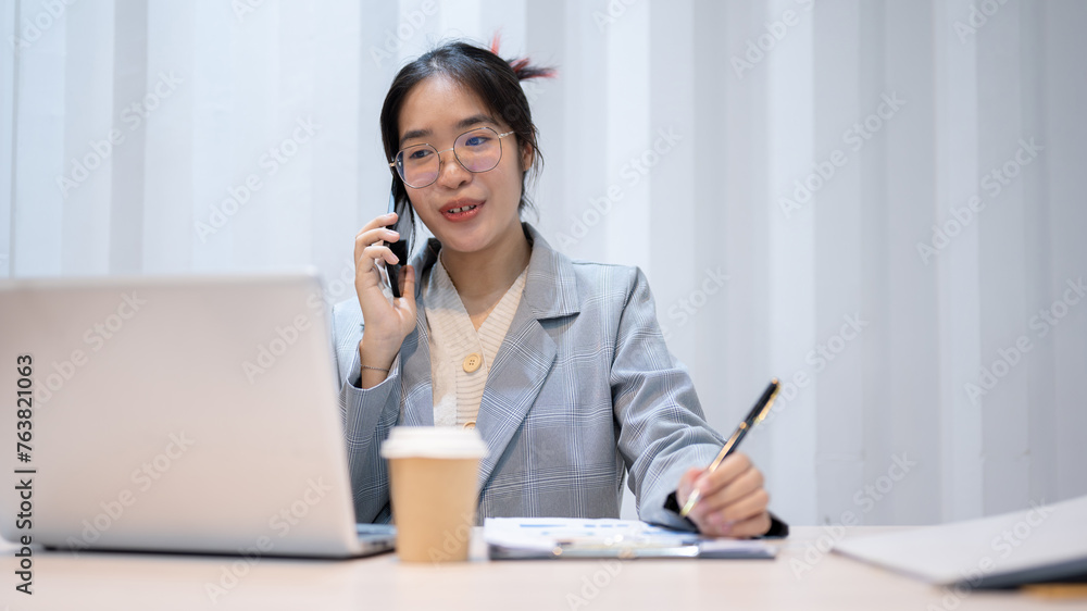 A confident Asian businesswoman is talking on the phone with her client while working in her office. A confident Asian businesswoman is talking on the phone with her client while working in her office.