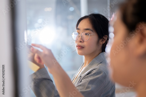 A businesswoman brainstorming and reading some ideas on sticky notes on a glass wall with her team.