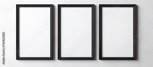 Three rectangular black frames are symmetrically hanging on a monochrome white wall, creating a pattern with parallel lines. The frames symbolize elegance and simplicity with their metal finish
