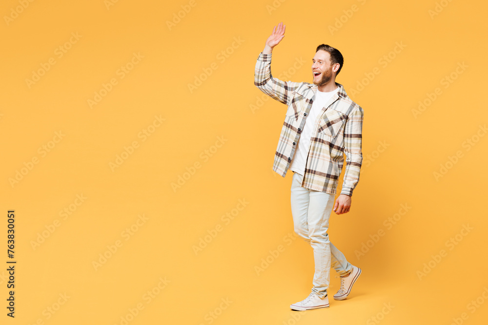 Fototapeta premium Full body side profile view young smiling happy Caucasian man he wear brown shirt casual clothes waving hand walking going isolated on plain yellow orange background studio portrait Lifestyle concept
