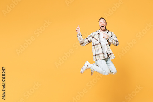 Full body young happy Caucasian man he wear brown shirt casual clothes jump high point index finger aside on area mock up isolated on plain yellow orange background studio portrait. Lifestyle concept. © ViDi Studio