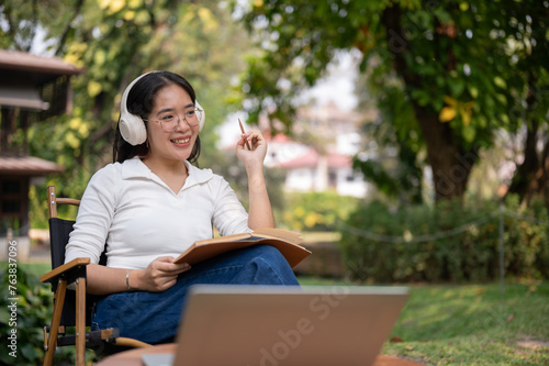 Happy Asian woman is listening to music, working or writing her diary while sitting in her backyard.