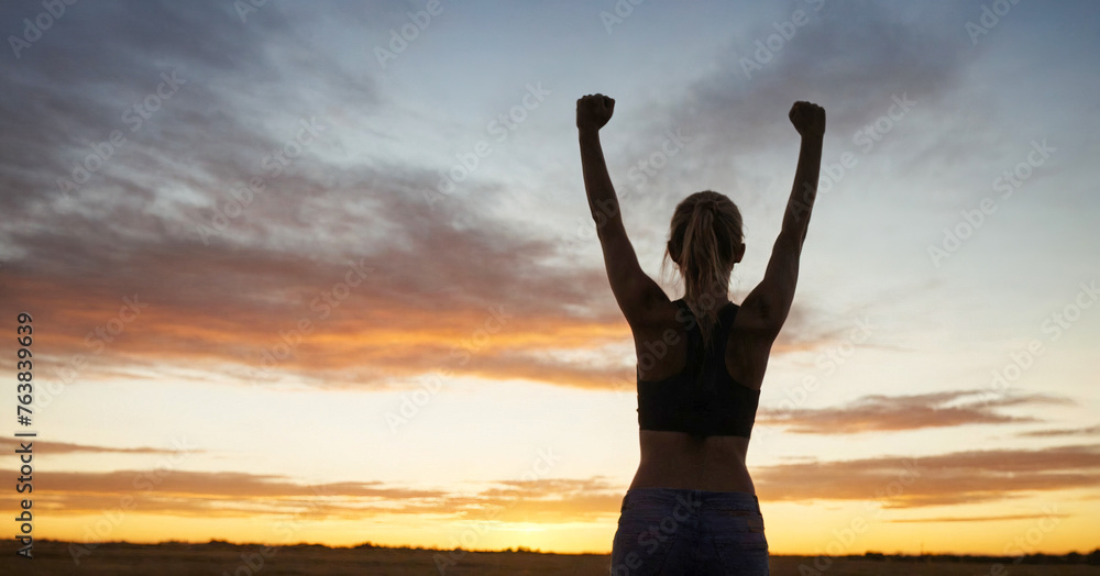 Silhouette of confident woman raising her hands in triumph against sunny sky, symbolizing success and empowerment.