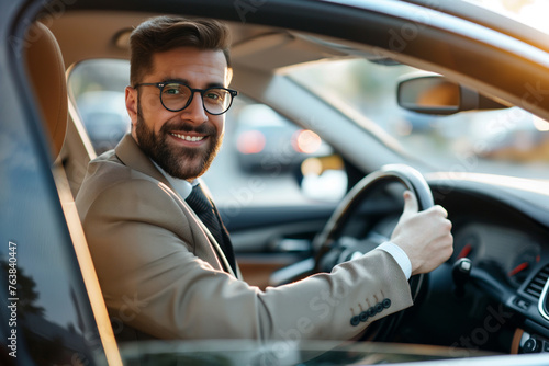 likeable businessman with suit and beard sits in the car at the steering wheel and smiles into the camera - topic company car and driver's license © Steffen Kögler