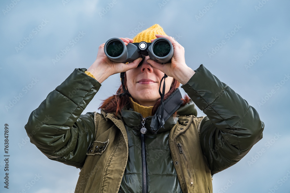 female ornithologist birdman watches birds with binoculars on dirt gravel road against a background of a stormy sky female ornithologist birdman watches birds with binoculars on dirt gravel road against a background of a stormy sky