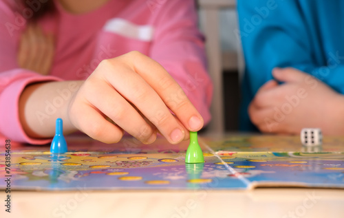 Board game and children's leisure concept - little child's hand holds green piece in its hand over game board. Selective focus.