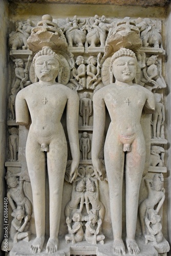 A finely detailed stone sculpture of a  Jain Tirthankara ADINATH,  with a serene expression, surrounded by ornate carvings 
