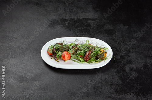 Salad with boiled octopus, potatoes and vegetables with pesto sauce on black stone background. Octopus salad with greens and potatoes in ceramic plate. 
