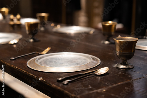 Antique dining set with golden cups and silverware on a vintage wooden table, conveying a sense of historical elegance