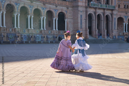 Two girls dancing flamenco walking and talking happily, with their backs turned, in typical flamenco costume in a nice square in Seville. Dance concept, flamenco, typical Spanish, Seville, Spain.