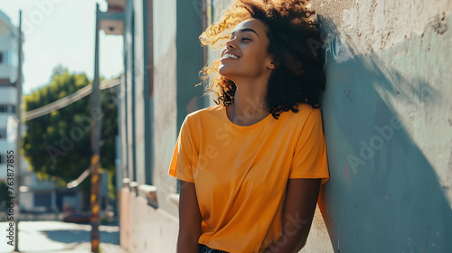 striking mockup featuring a black happy woman in an orange t-shirt standing on a vibrant city street, exuding confidence and urban style. blue wall