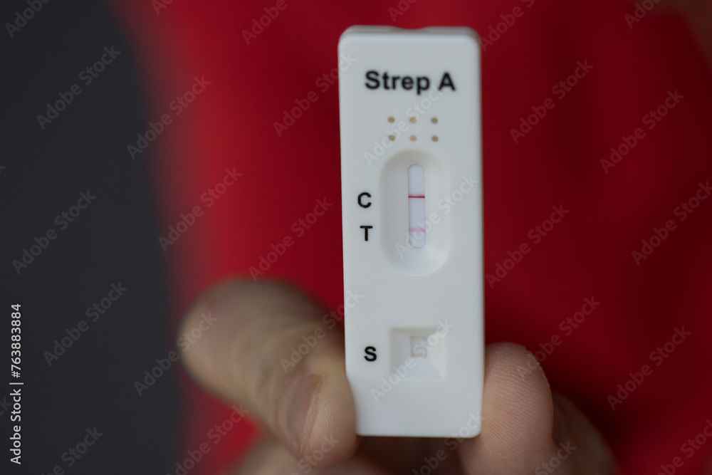Close-up of hand holding positive streptococcus test during infection, diagnostic test done at home for telephone consultation with doctor. Close-up of hand holding positive streptococcus test during infection, diagnostic test done at home for telephone consultation with doctor.