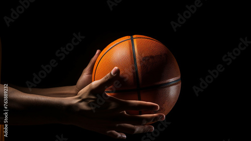 A basketball player's hand holding a basketball on dark background © Yuwarin