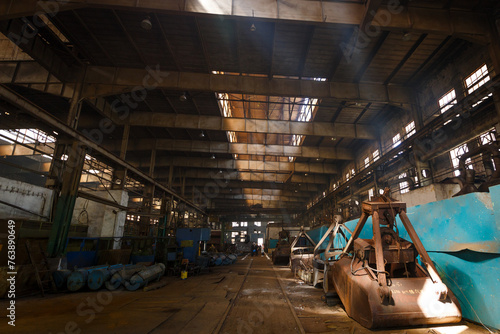 Abandoned industrial warehouse with rusty machinery, old equipment scattered, sunlight piercing through roof. Derelict factory interior, urban exploration, decaying infrastructure, sunlight beams.